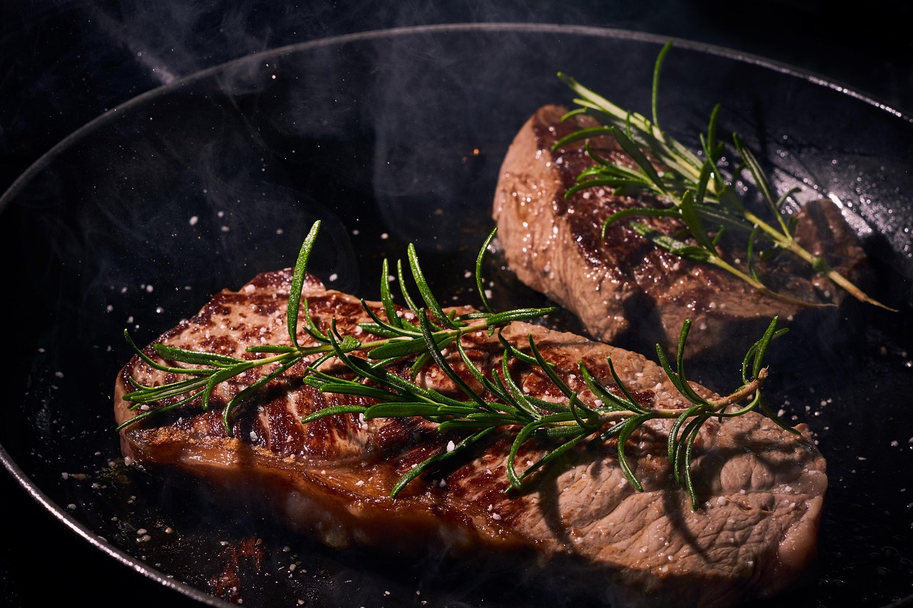 Zwei perfekt gebratene Straußensteaks in dunkler Pfanne mit Rosmarinzweigen im MAHABU Blog.